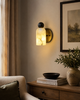 Sloane Rounded Alabaster Wall Sconce installed in a contemporary living room, providing warm ambient lighting beside a wooden console and neutral décor.