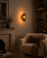 Solene Shield Wall Sconce installed in a cozy living room beside fireplace, shelves, and lounge chair.
