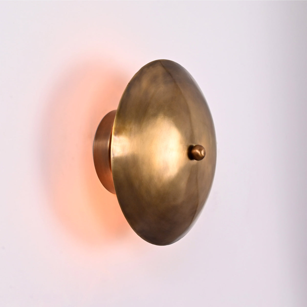 Solene Shield Wall Sconce shown from side angle with rounded disc shade and soft warm back glow.