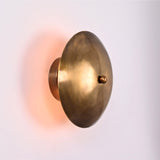 Solene Shield Wall Sconce shown from side angle with rounded disc shade and soft warm back glow.