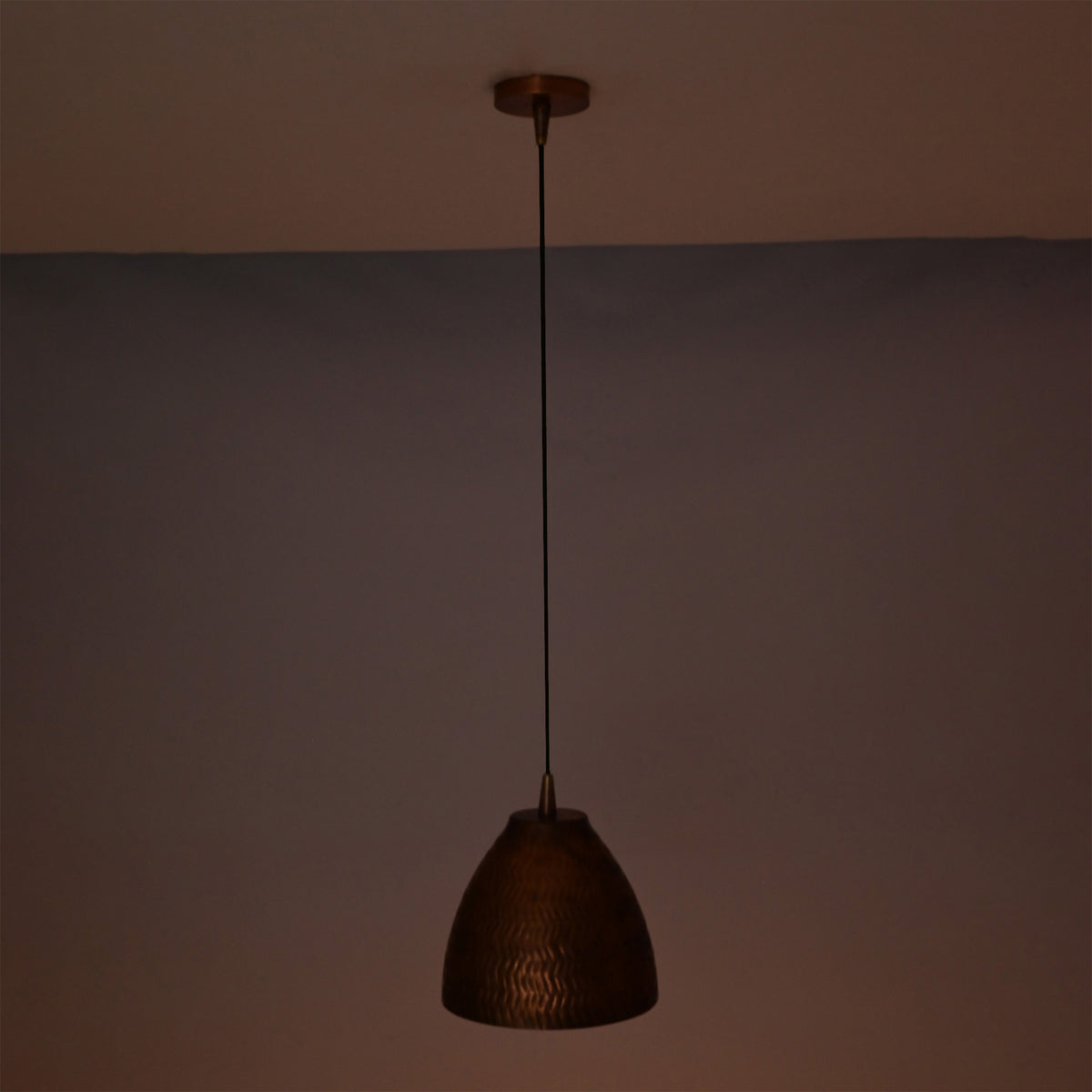 Sutton hammered bell pendant light casting a soft warm ambient glow while suspended from an adjustable black cord.