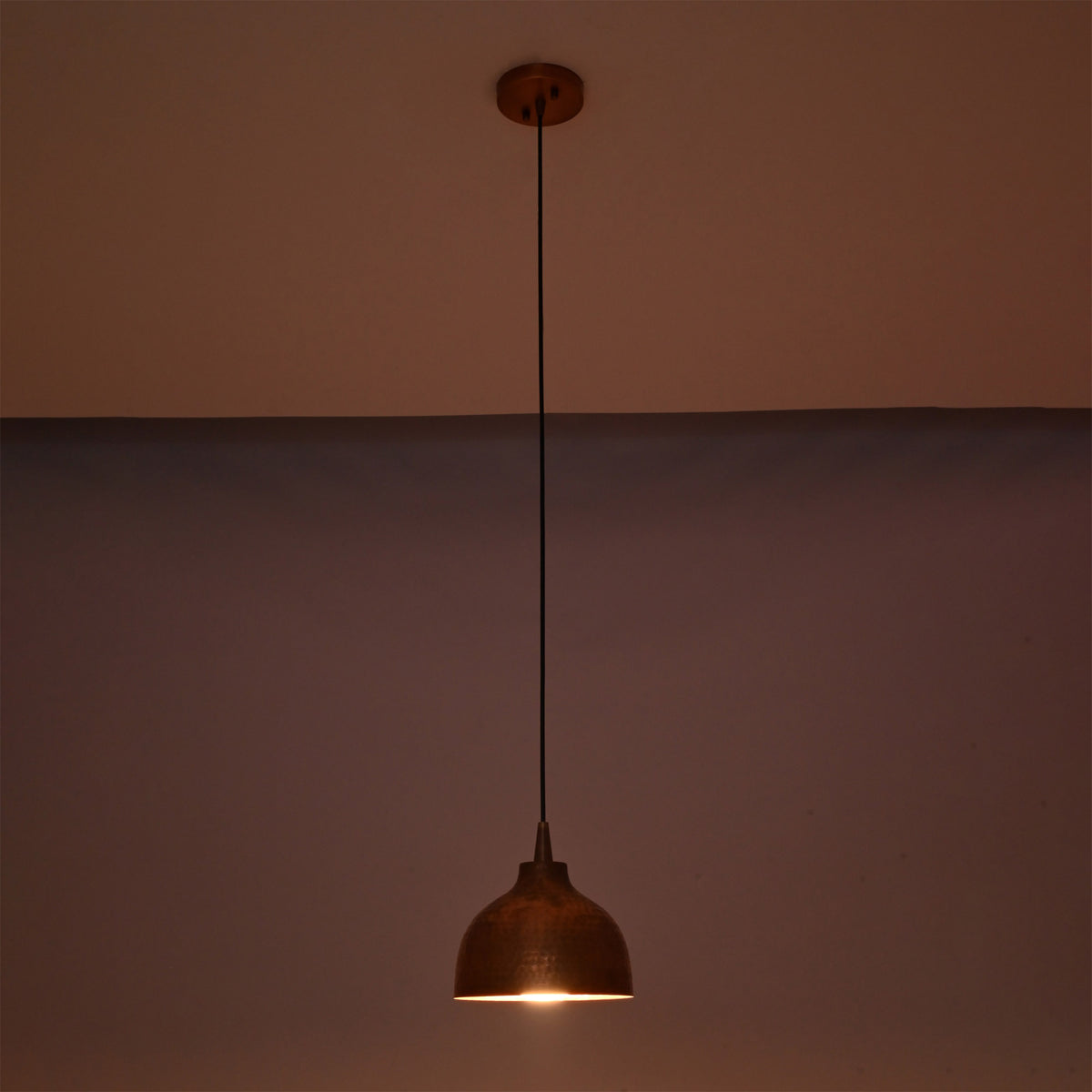 Sutton hammered copper mini dome pendant light casting a warm focused glow with textured copper shade in a dark setting.
