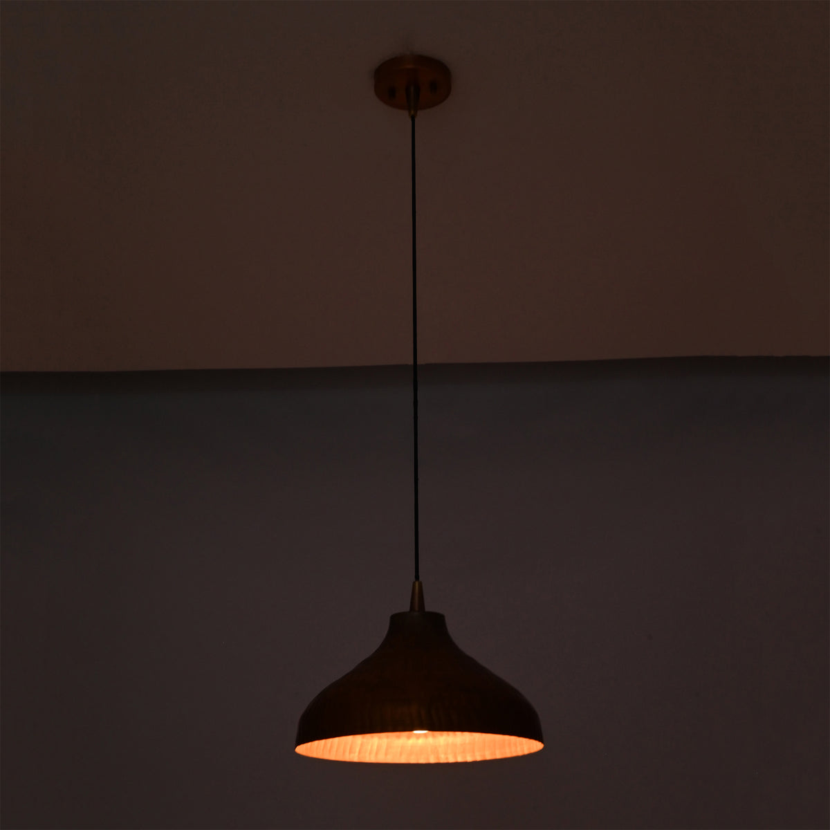 Sutton hammered copper dome pendant light casting focused downward illumination with a warm interior glow.