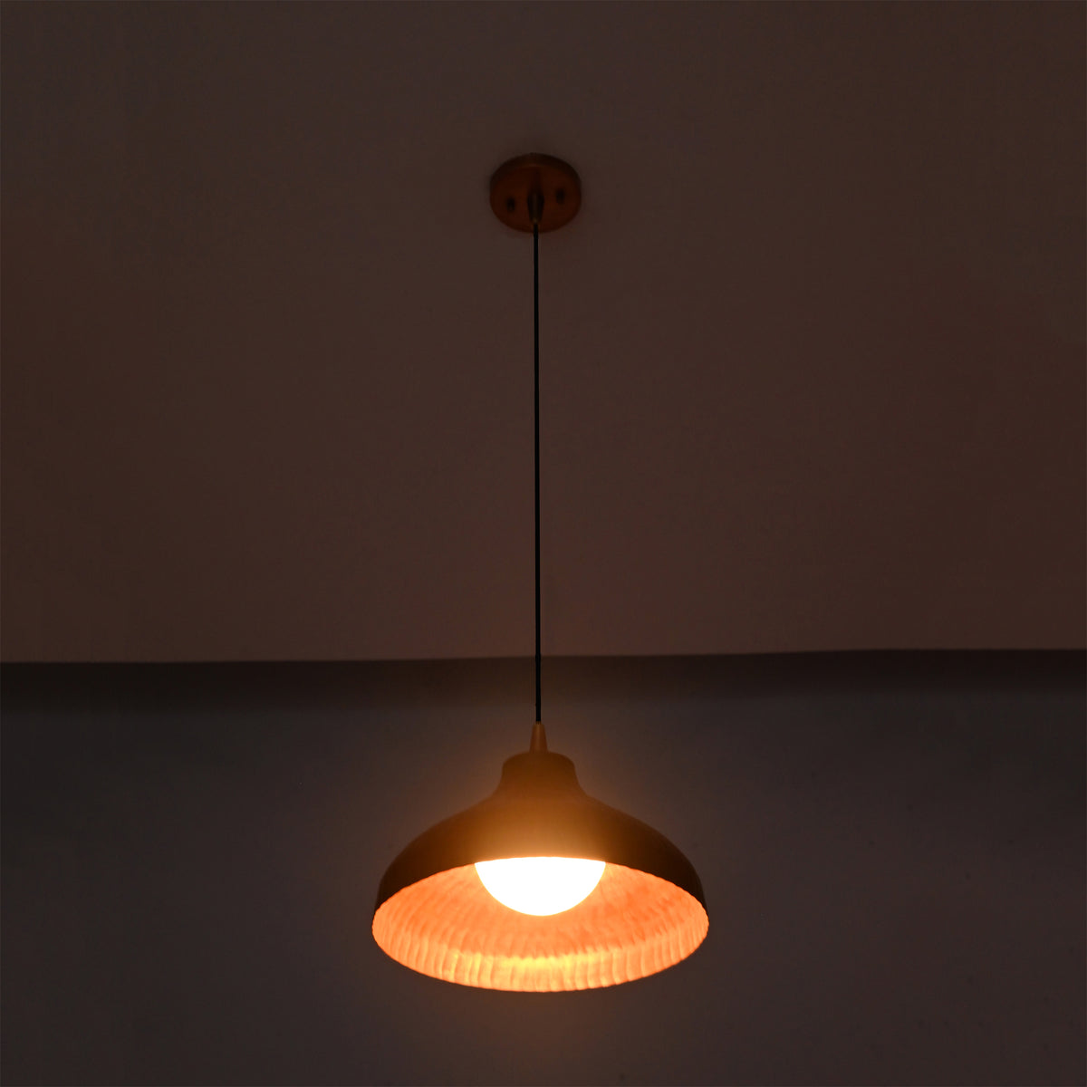 Detailed view of Sutton hammered copper pendant light with illuminated globe bulb and textured handcrafted dome shade.