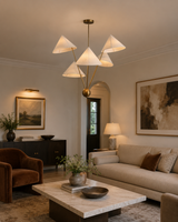 Sutton Modern five-light cone chandelier installed in a contemporary living room, providing warm ambient illumination with white fabric shades and a brushed brass frame.