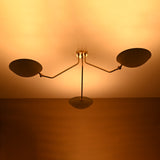 Warm glowing brass chandelier with three white shades viewed from below, handmade minimalist ceiling design