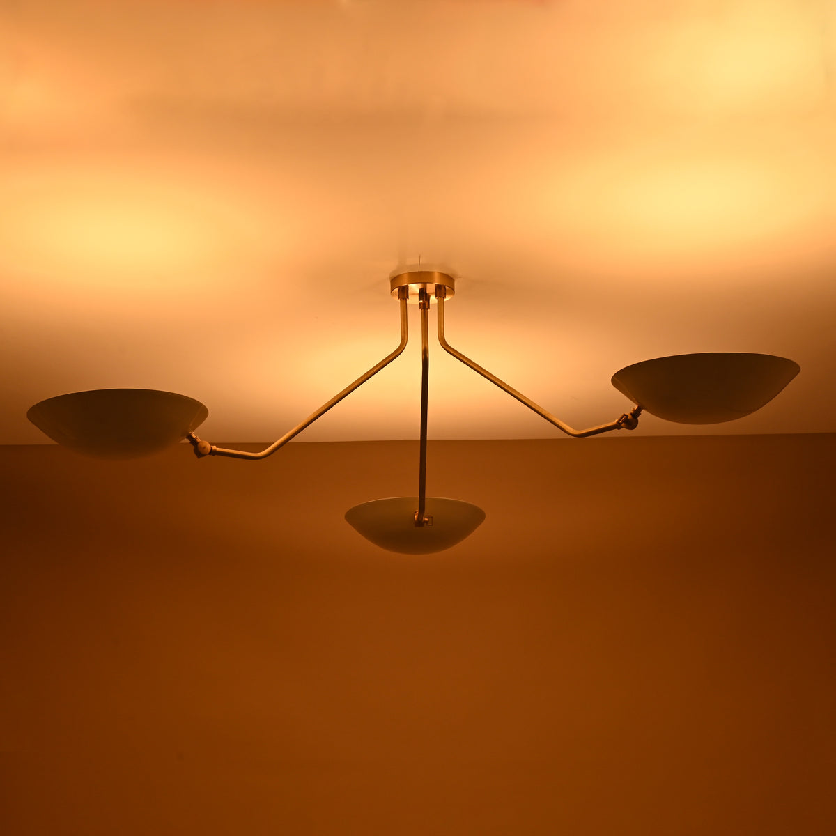 Illuminated three-light brass chandelier with white shades creating warm ambient glow on ceiling