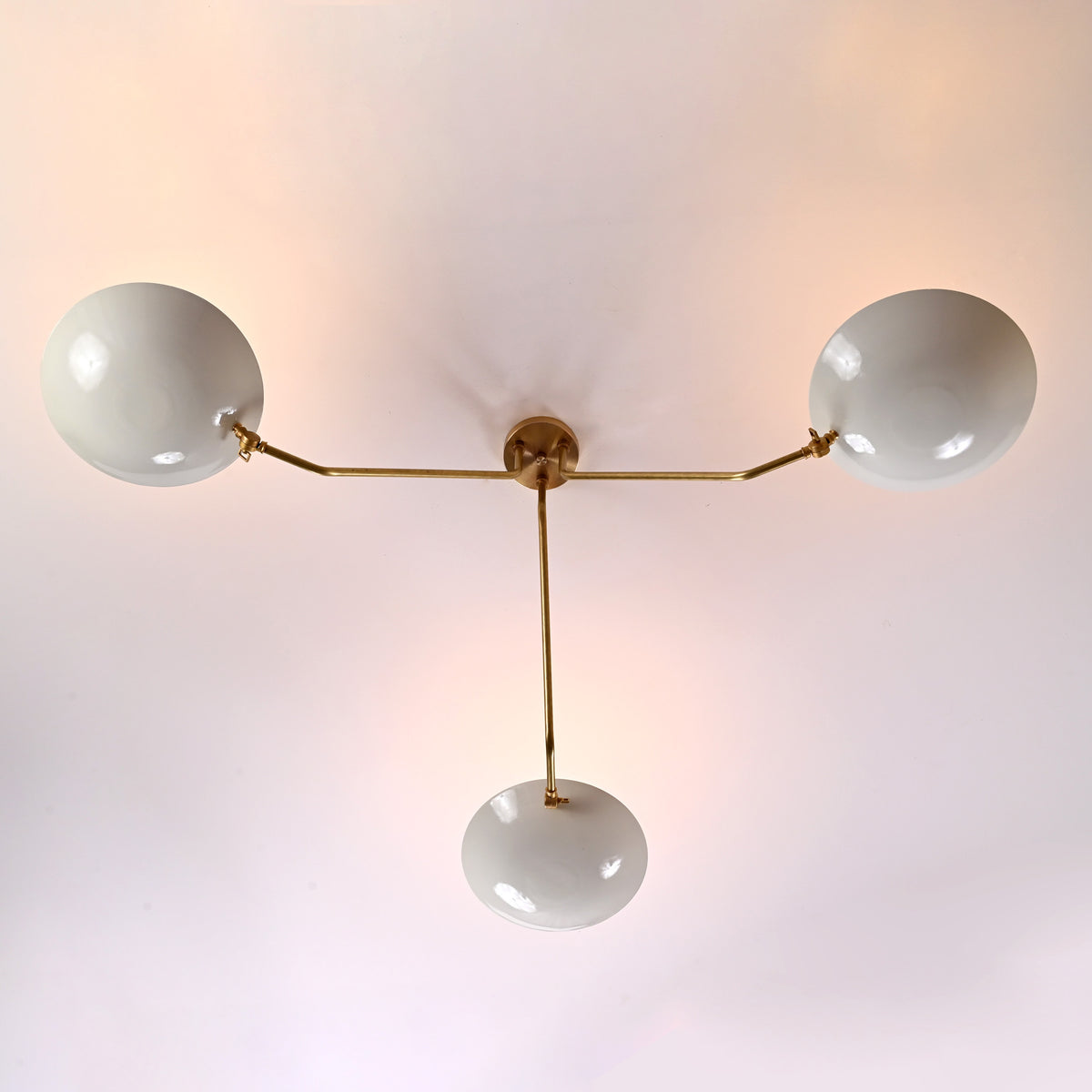 Overhead view of three-light brass chandelier with curved white bowl shades in minimalist design