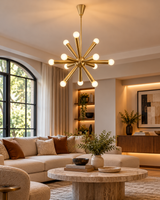 Illuminated Tokyo 12-light brass Sputnik chandelier hanging above a cream sectional sofa and round marble coffee table in an elegant contemporary living room with warm ambient lighting.