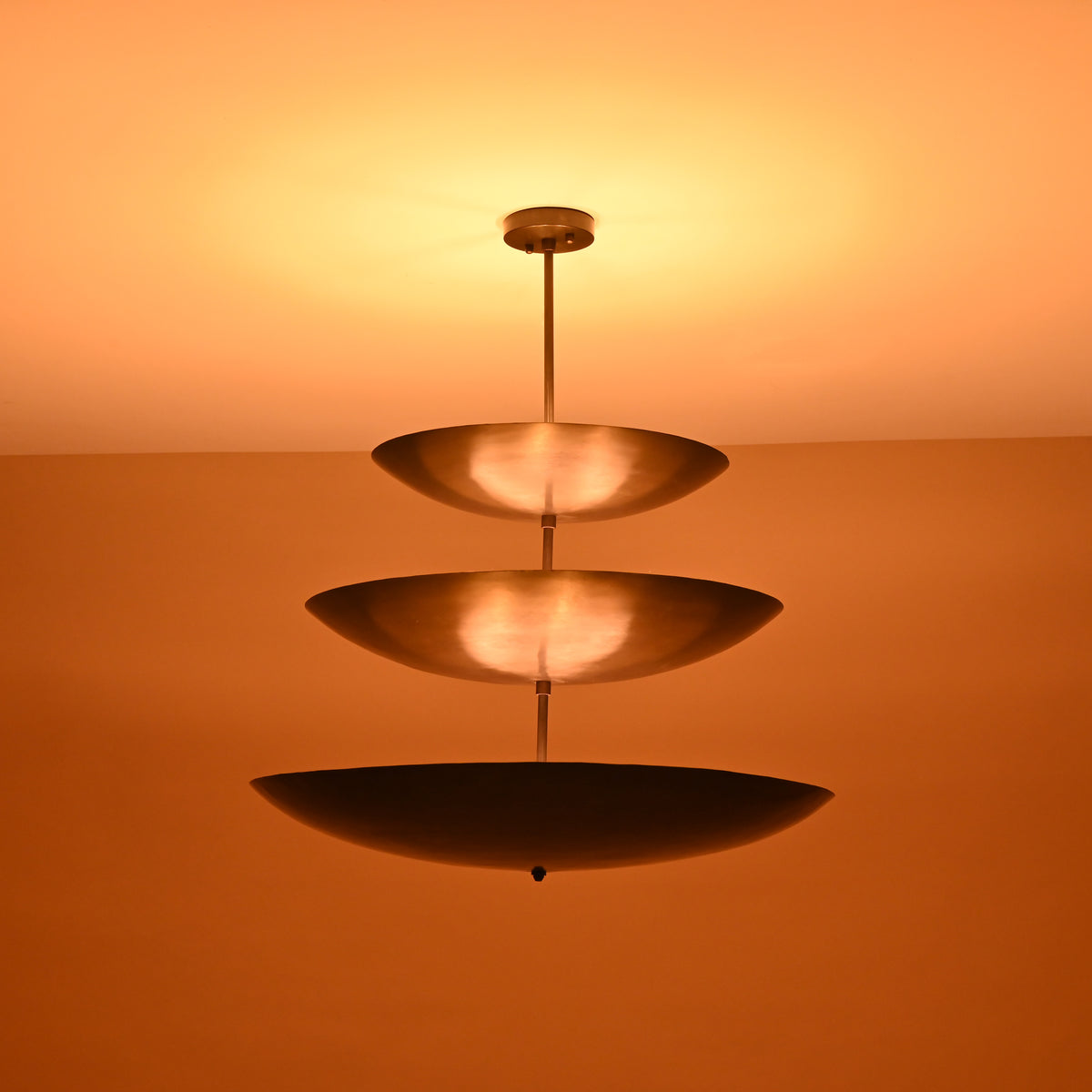 Close-up of illuminated triple bowl chandelier in blackened brass finish, showcasing soft indirect light