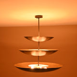 Full view of three-tier chandelier in blackened brass, glowing warmly with indirect upward illumination