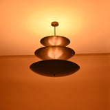 Wide shot of lit three-tier blackened brass chandelier casting ambient glow on ceiling