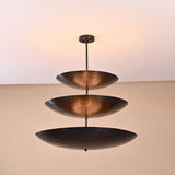 Three-layer brass chandelier in blackened finish viewed from side, minimalist industrial ceiling light