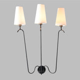 Modern three-arm wall sconce with sleek black metal frame and white fabric shades, mounted on a round base for elegant ambient lighting.