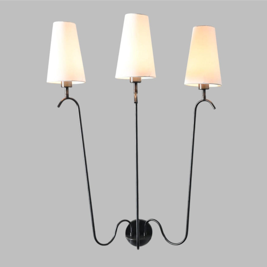 Modern three-arm wall sconce with sleek black metal frame and white fabric shades, mounted on a round base for elegant ambient lighting.