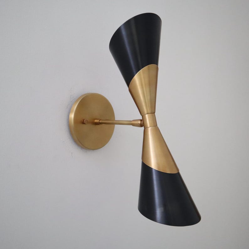 Angled left view of two tone brass and black double cone wall sconce with round brass backplate on a light wall.