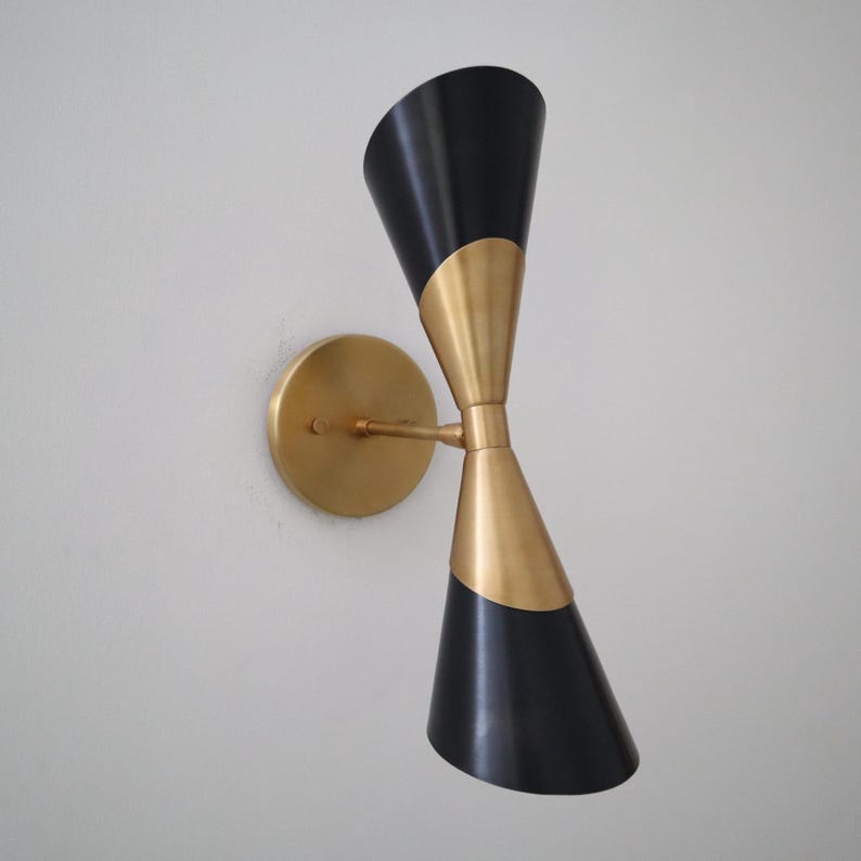 Side perspective of two tone double cone wall sconce in black and brass mounted on a round brass wall plate.