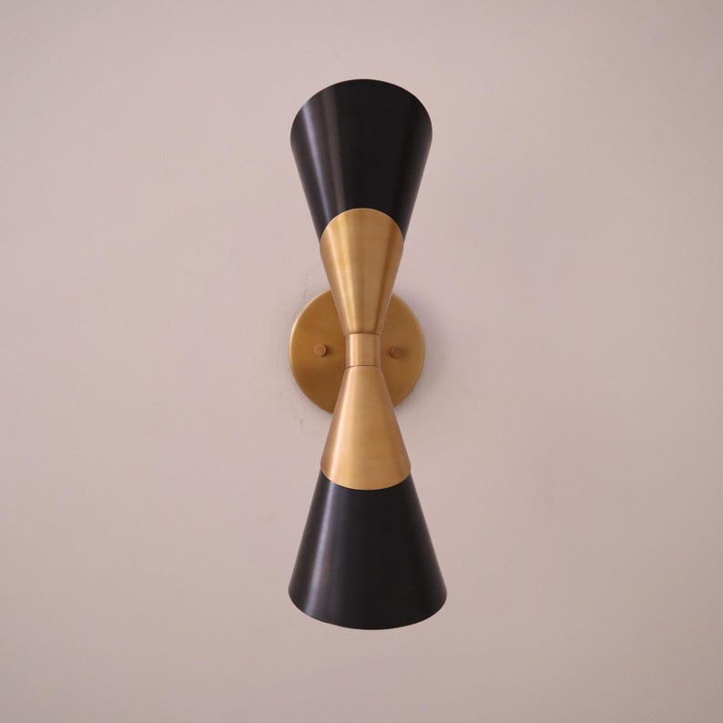 Straight on front view of two tone brass and black double cone wall sconce centered on a light wall.