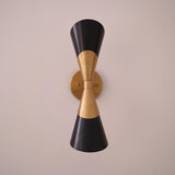 Straight on front view of two tone brass and black double cone wall sconce centered on a light wall.