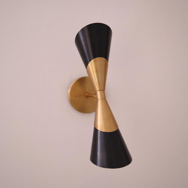 Three quarter view of brass and black double cone wall sconce showing both cone shades and the brass mounting plate.