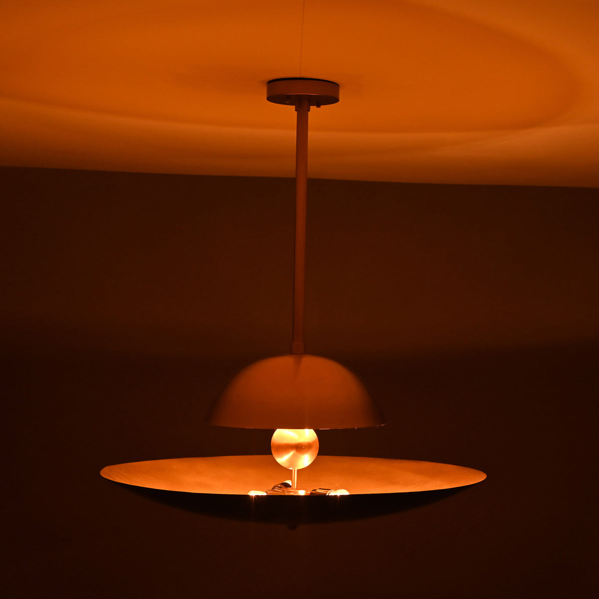 Venice Disc pendant shown illuminated, casting a warm glow through its sculptural layered shade profile.