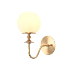 Verona Modern Globe Glass Wall Sconce glowing warmly with decorative turned stem and curved brass arm in a three-quarter perspective.