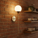Lit Verona globe balance wall sconce with warm glowing glass globe and elegant antique brass frame.