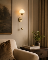 Verona globe balance wall sconce with antique brass finish and illuminated glass globe styled in an elegant living room.