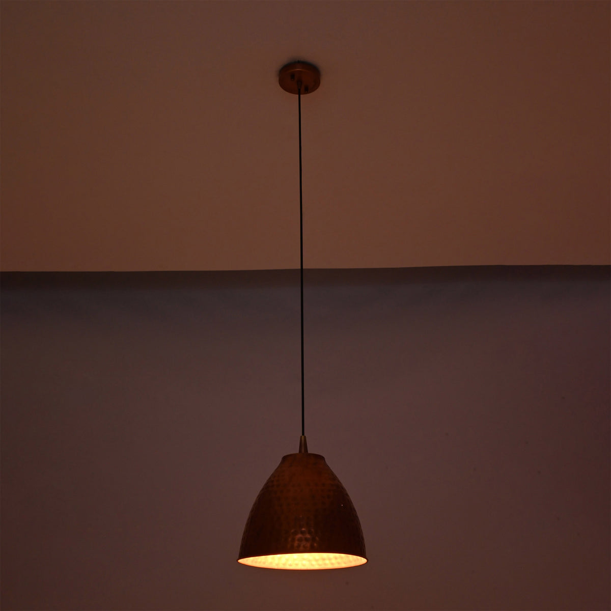 Verona hammered copper bell pendant light suspended in a dark setting with warm focused downward illumination and a handcrafted hammered copper shade.