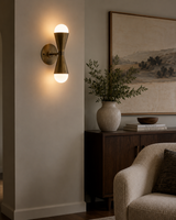 Verona hourglass globe wall sconce installed in a contemporary living room, providing warm ambient lighting above a wooden console in a modern interior.