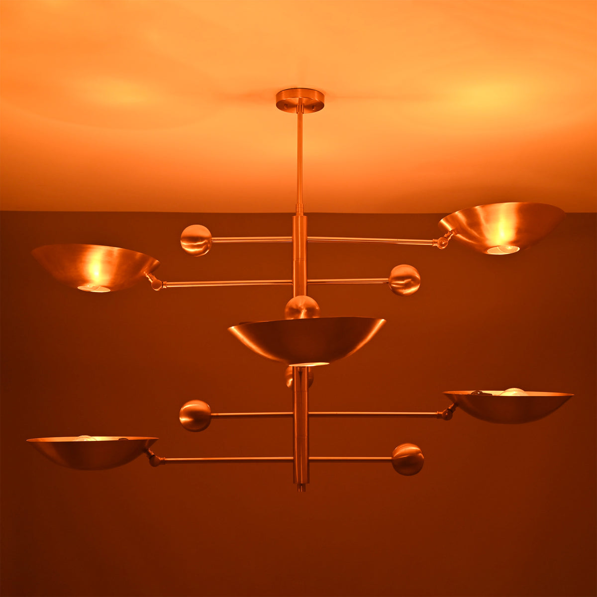 Verona Orbital chandelier shown illuminated, casting warm light through sculptural bowl shades and offset arms.