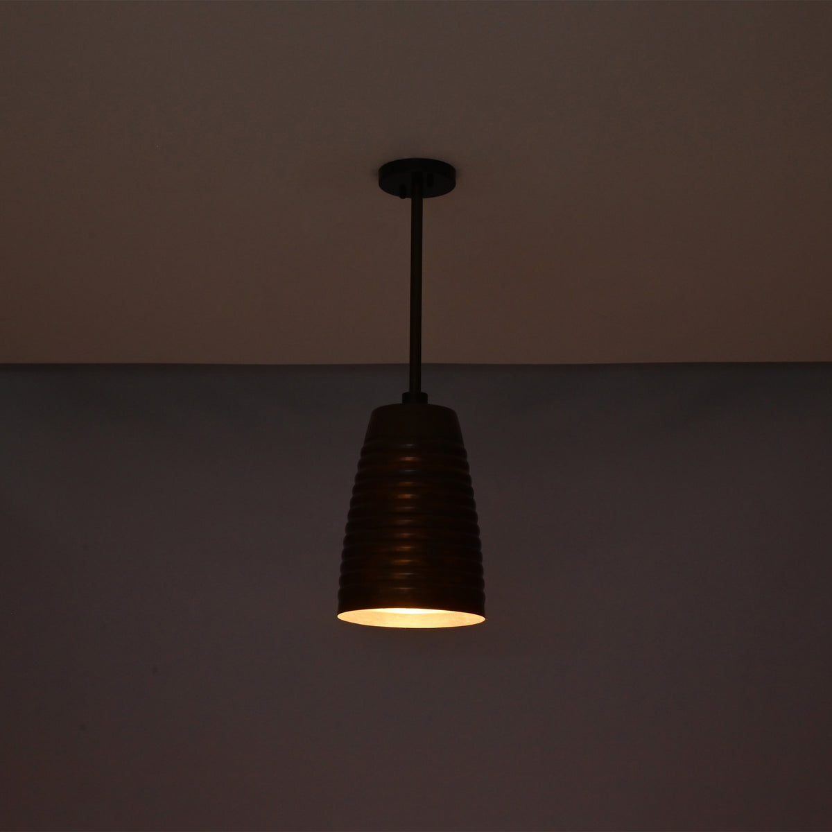 Night view of the Verona ribbed bell pendant light suspended from the ceiling with warm focused illumination and handcrafted ribbed copper shade.
