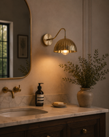 Verona ribbed brass dome wall sconce illuminated above a bathroom vanity with warm ambient lighting.