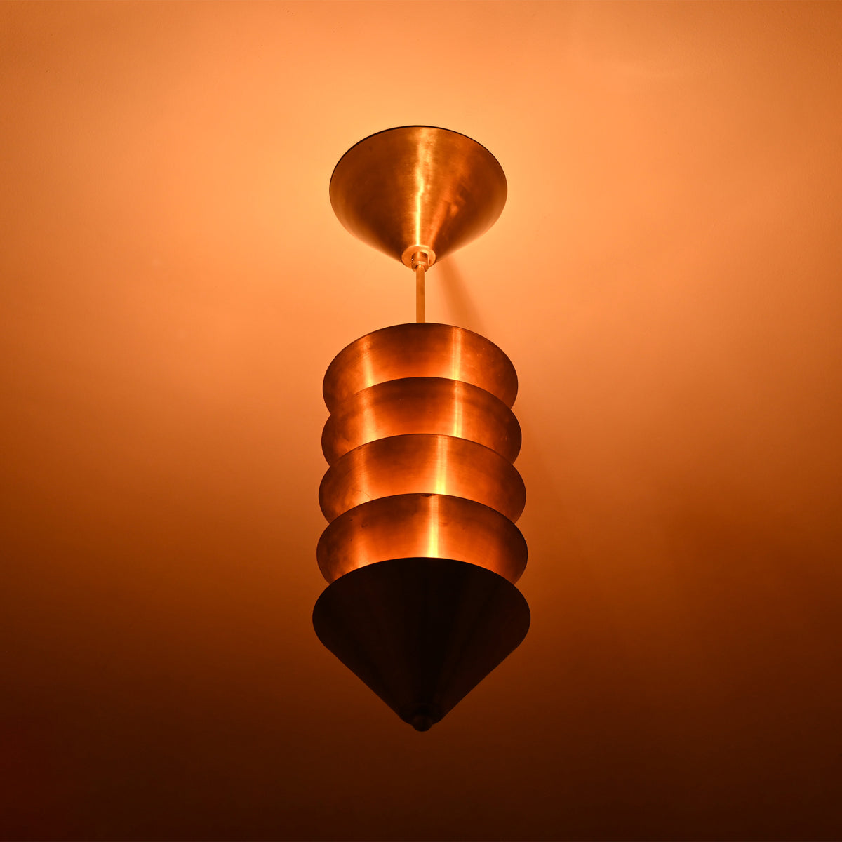Verona Stacked Cone Pendant close ceiling view showing layered cone shades and dramatic warm lighting.