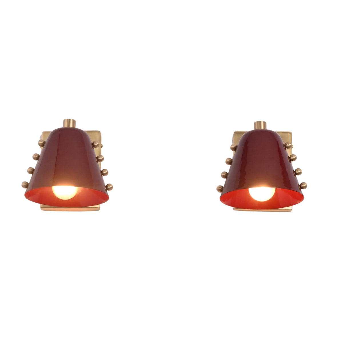 Verona Studded Cone Wall Sconce illuminated with a warm glowing bulb beneath a handcrafted burgundy cone shade accented with decorative brass studs.