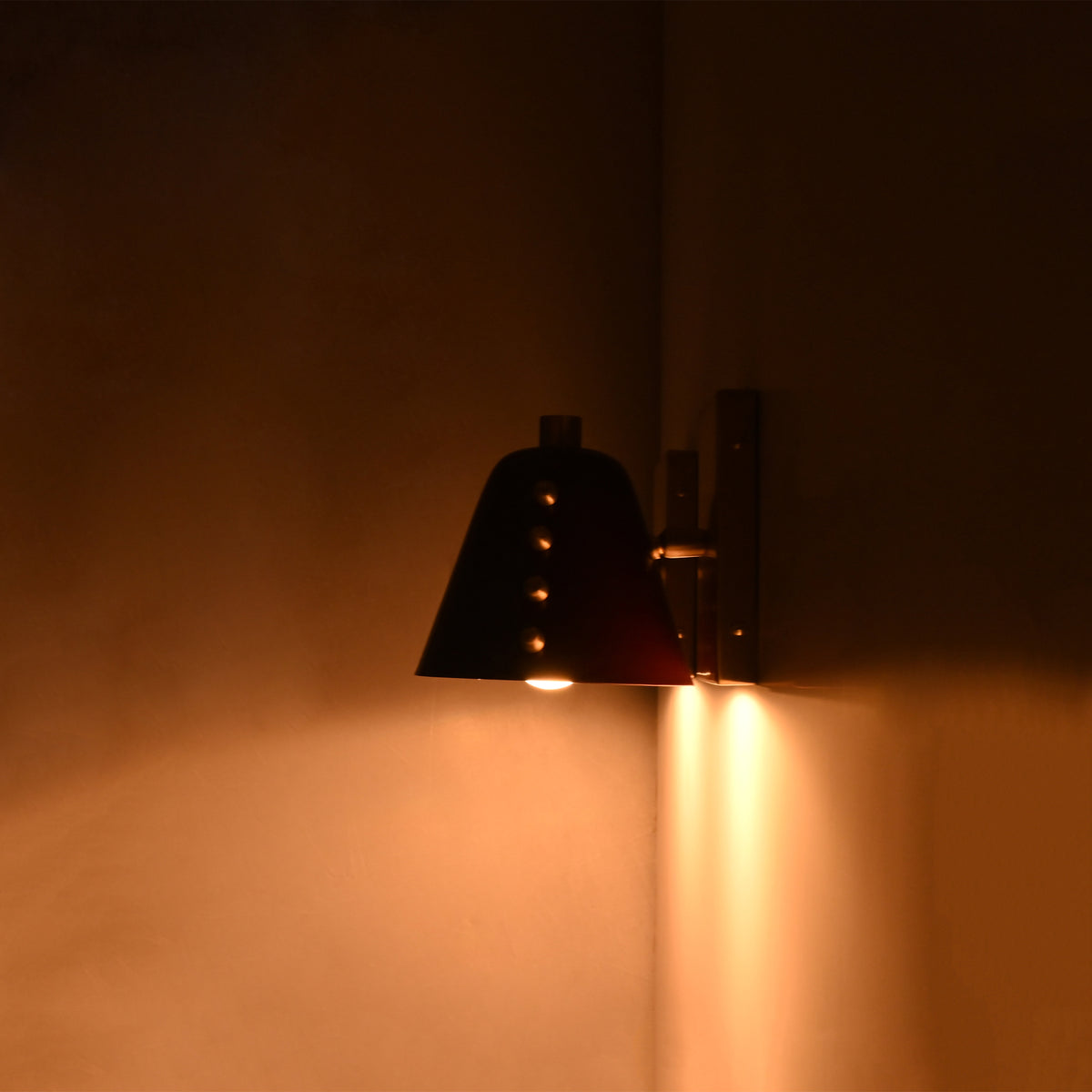Verona Studded Cone Wall Sconce illuminated at night, casting warm downward ambient light with its handcrafted burgundy cone shade and brass detailing.