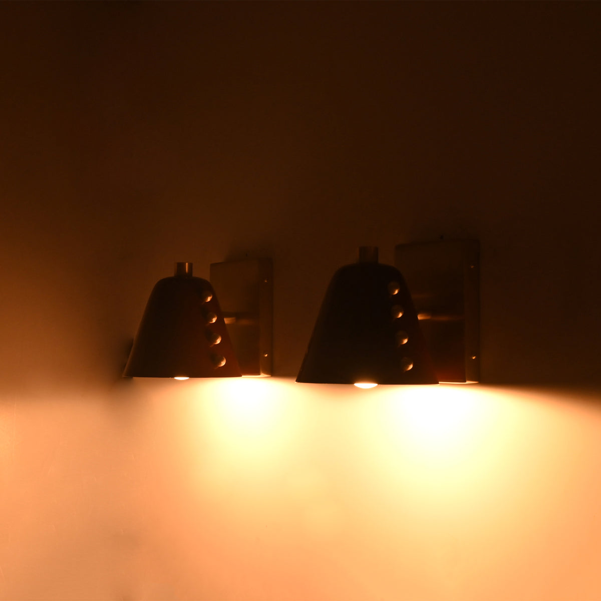 Pair of Verona Studded Cone Wall Sconces providing warm ambient lighting on a wall, showcasing handcrafted burgundy cone shades with decorative brass studs.