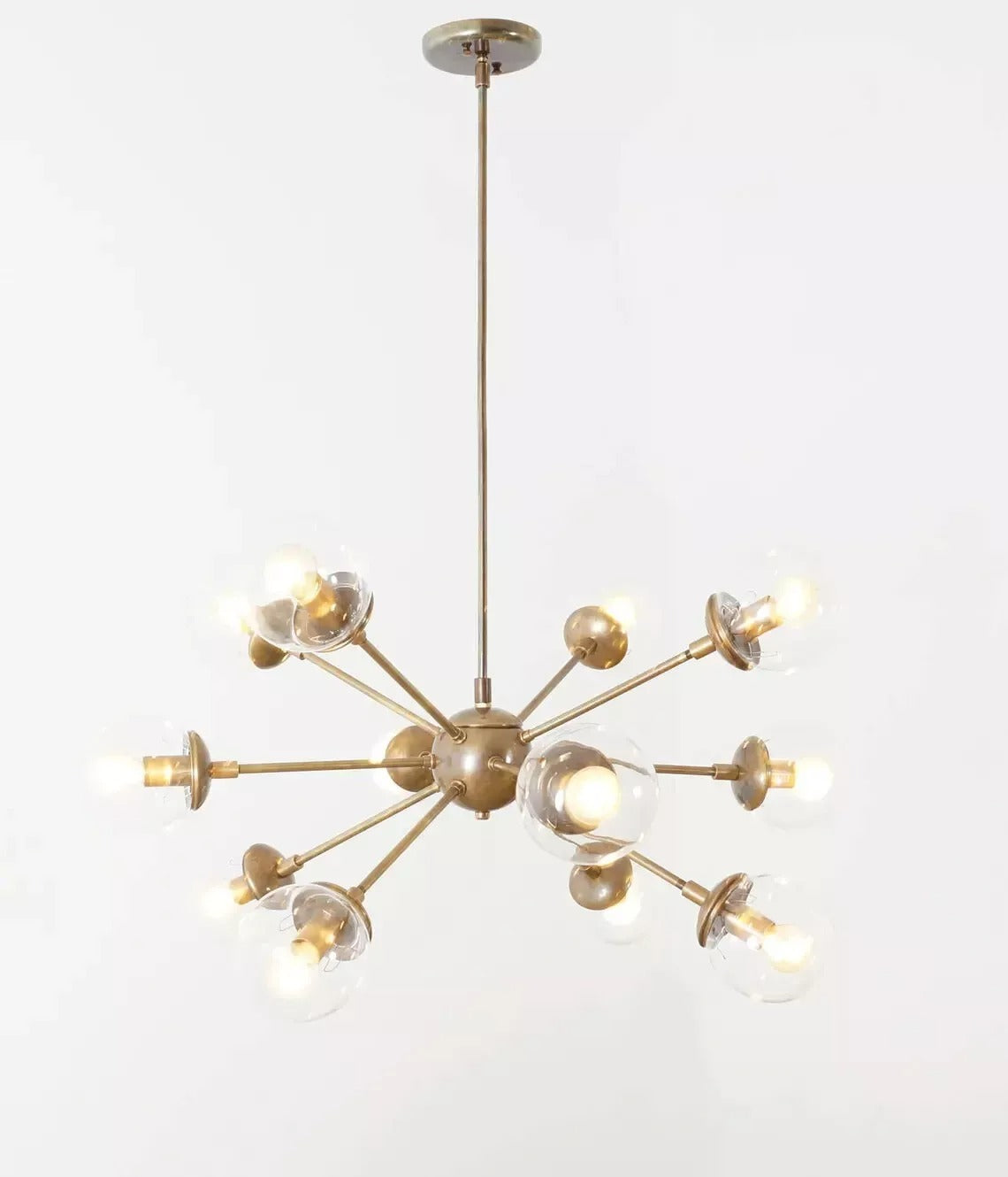 Full view of the Versailles 12 light chandelier featuring sculptural brass-tone radial arms and clear glass globe shades.