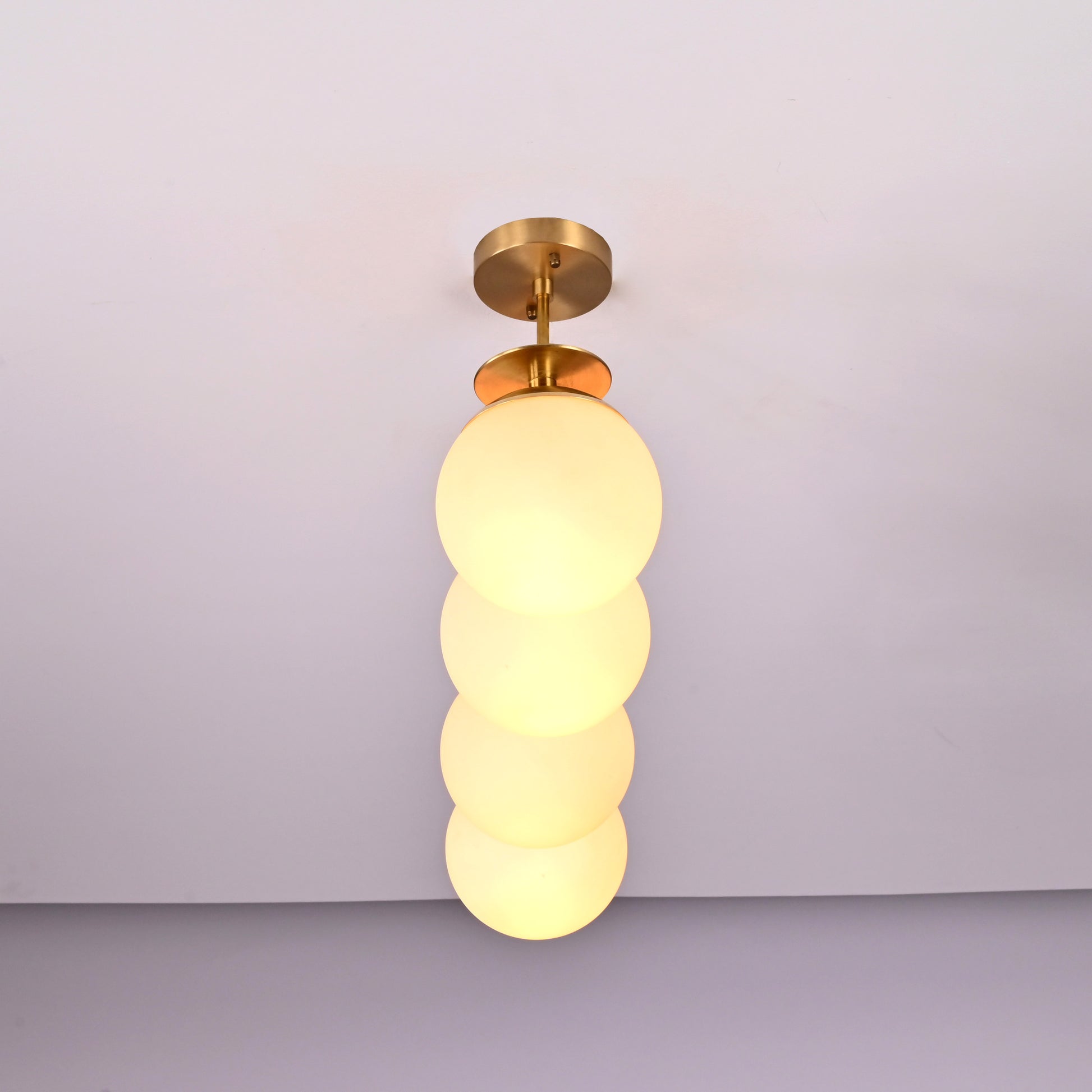 Handmade brass pendant light with four stacked frosted globes in vertical alignment, modern chandelier for hallways and entryways.