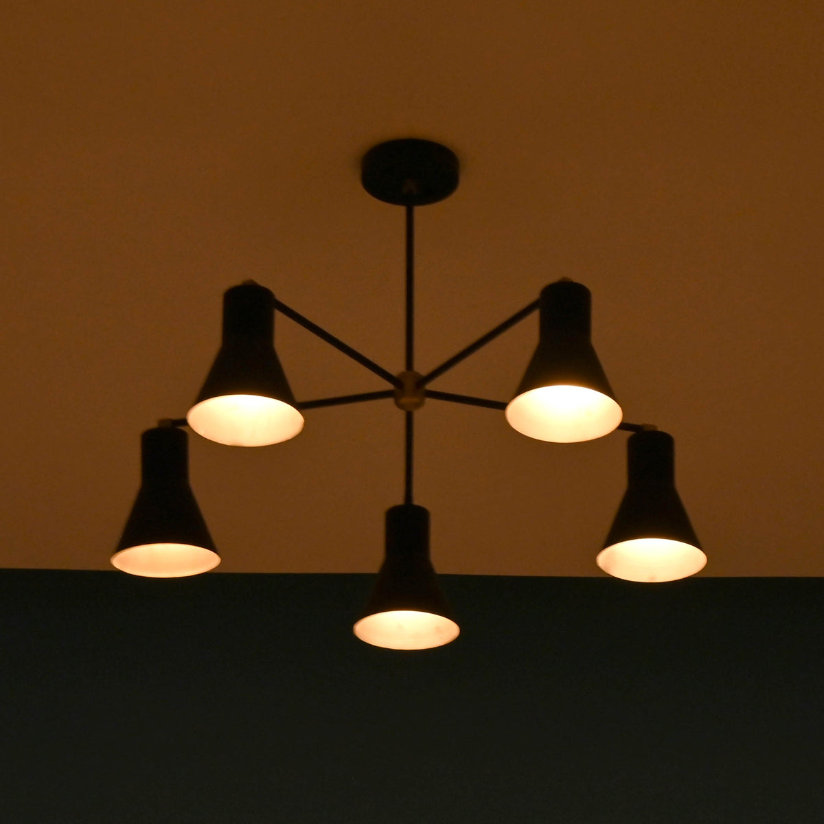 Five-light black chandelier glowing softly in a dim room, creating a cozy atmosphere.