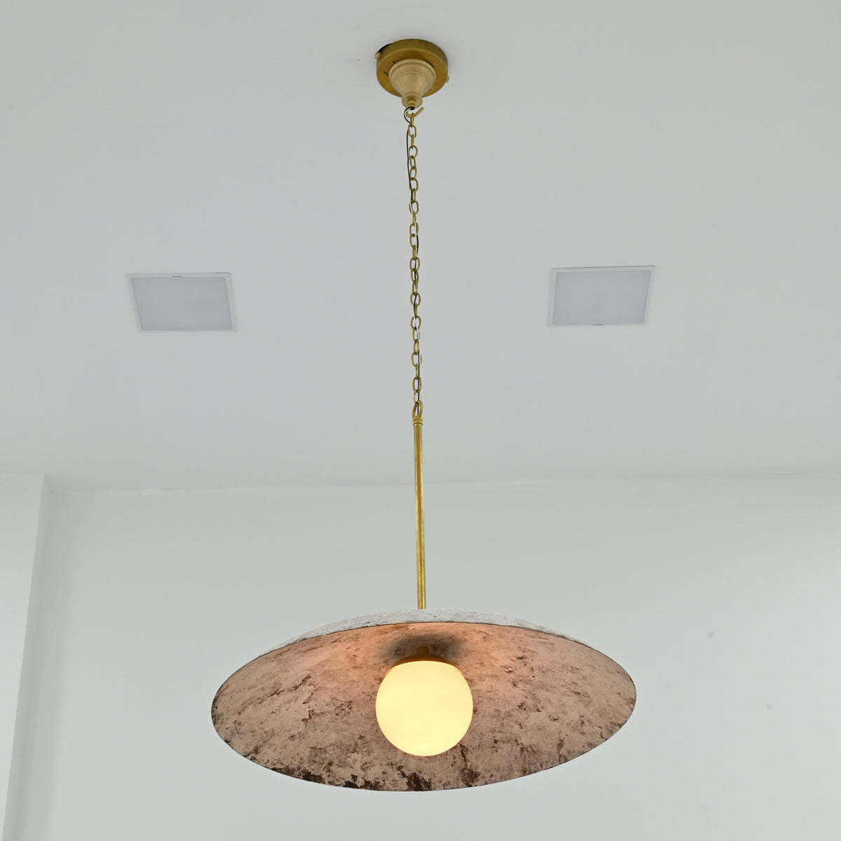 Wellington single light pendant featuring a distressed white dome shade, textured interior, brass hanging chain and illuminated globe bulb, viewed from below.