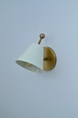 Minimalist white shade brass wall sconce angled view with round backplate and conical shade.
