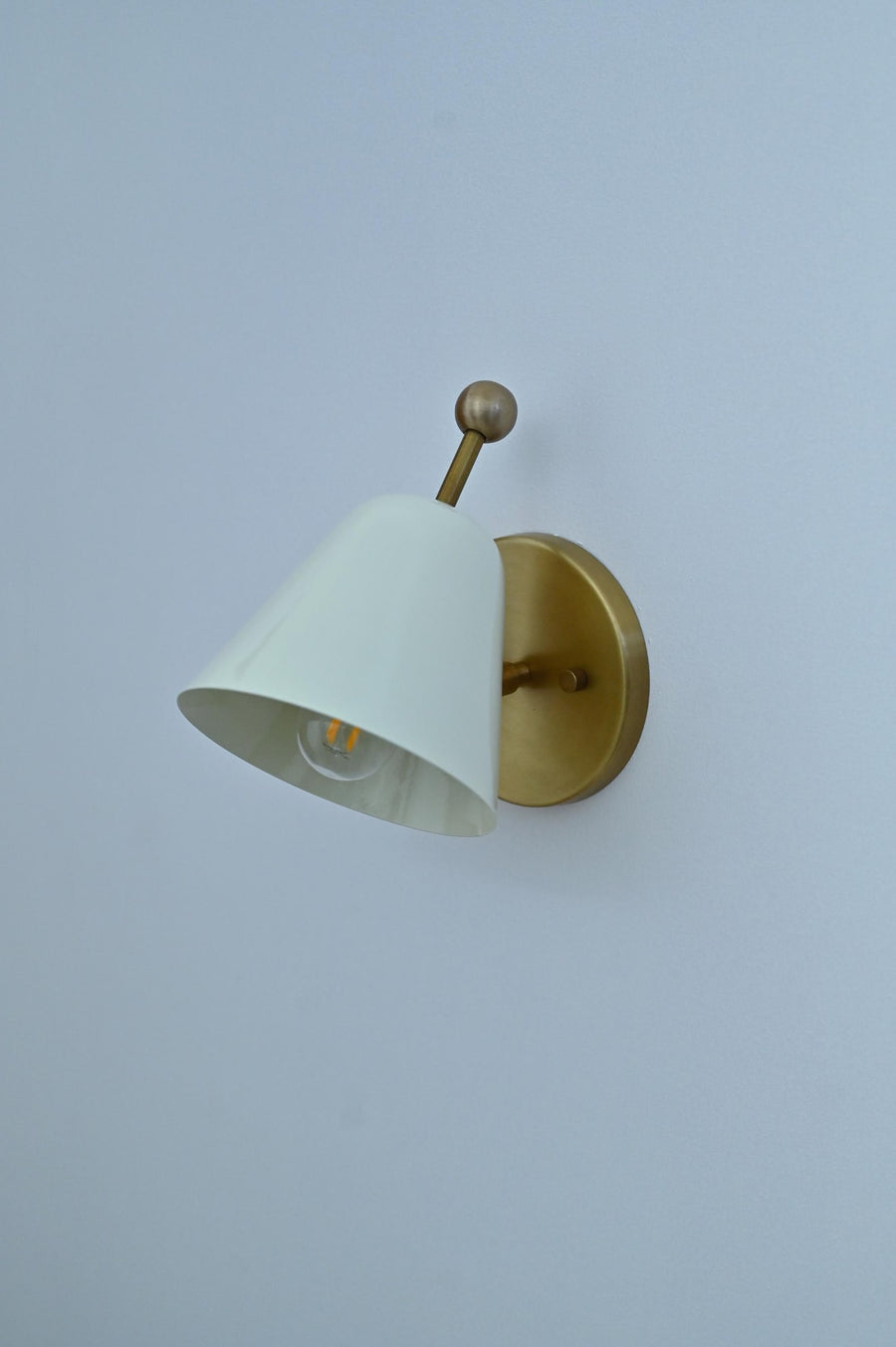 Minimalist white shade brass wall sconce angled view with round backplate and conical shade.