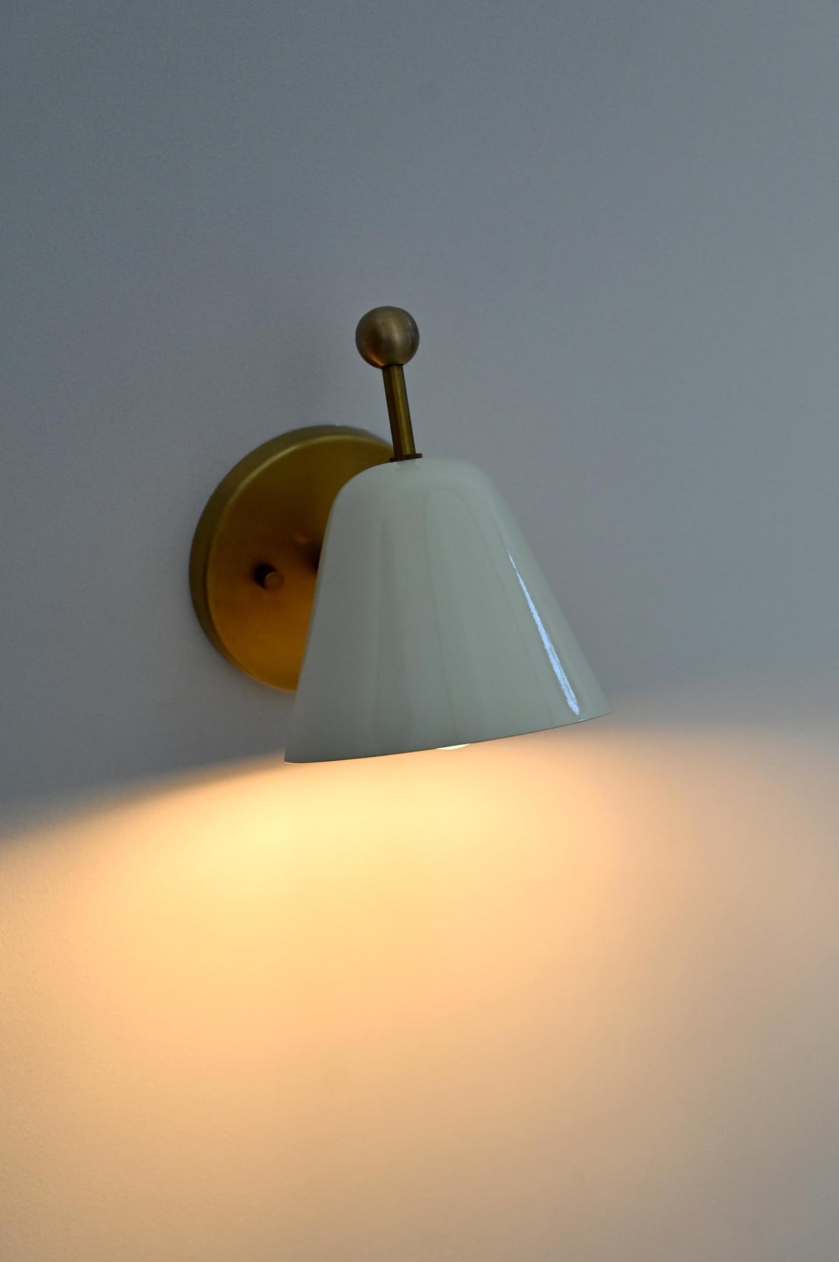 Close up of brass wall sconce with glossy white shade, lit with warm light.