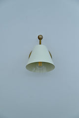 Front view of white conical shade brass wall sconce with exposed bulb inside.