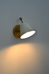 Brass wall sconce with white shade illuminated, casting warm ambient light on the wall.