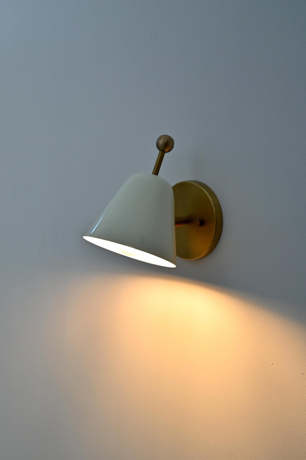 Side view of white brass wall sconce turned on, projecting warm downward glow.