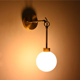 Angled installed view of the Windsor Modern Brass Globe Wall Sconce featuring a glowing frosted opal glass globe suspended from an elegant brass ring and stem.