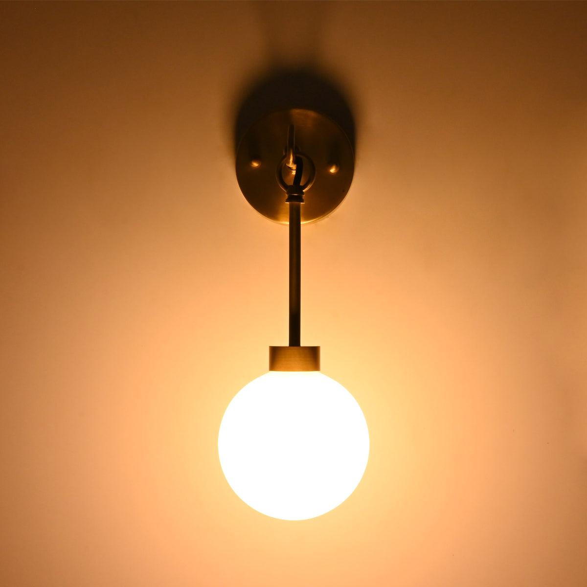 Front view of the Windsor Modern Brass Globe Wall Sconce mounted on a wall, providing soft ambient illumination through a frosted opal glass globe.