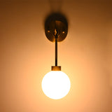 Front view of the Windsor Modern Brass Globe Wall Sconce mounted on a wall, providing soft ambient illumination through a frosted opal glass globe.